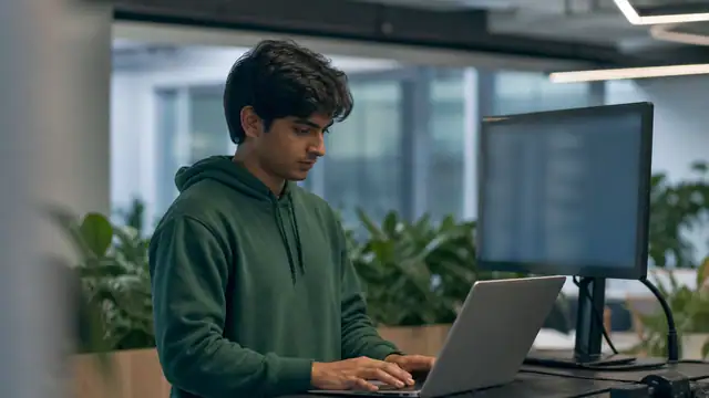 A graduate working at a laptop in an office.