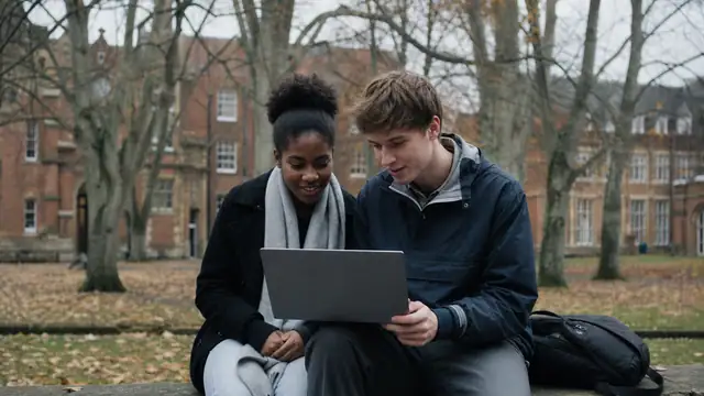 Two students looking at a laptop on a university quad.